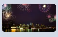 A nighttime photo of a city across a river with colorful fireworks in the sky