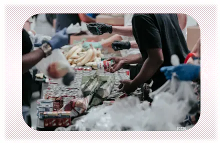 Many people stand around a table and pack food in bags