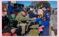 A young boy in a scouts uniform shakes the hand of an older man wearing a Veteran cap