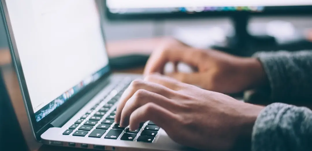 closeup of hands typing on open laptop keyboard