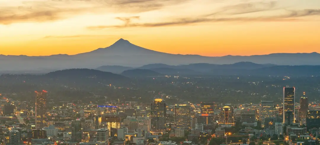 Landscape photo overlooking Portland, Oregon, at sunset, with a golden sky and hazy mountains in the background.