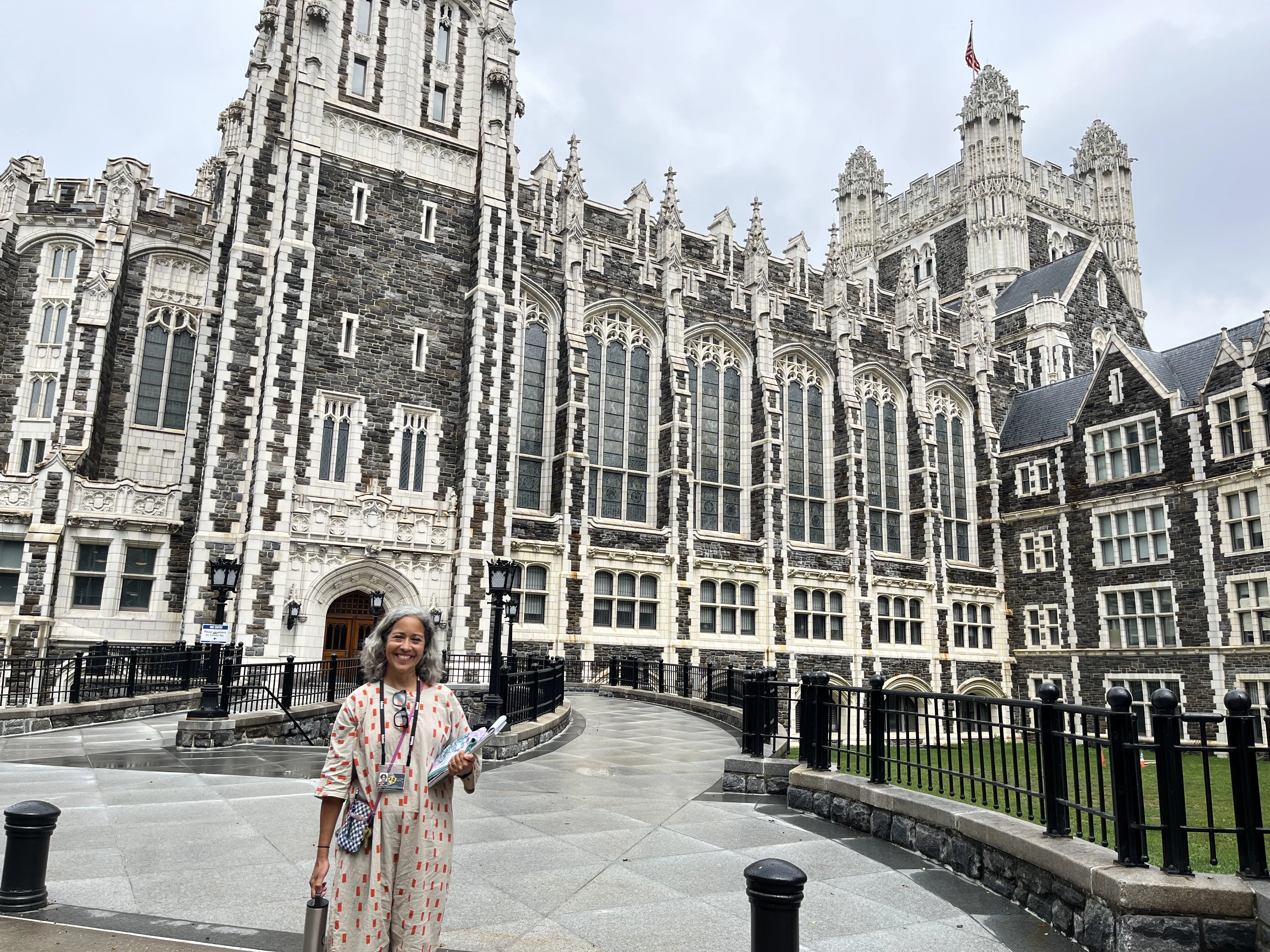 Dr. Block-Cora stands and smiles in front of Shepard Hall, a main building at City College of New York, built in spectacular New Gothic Revival style.